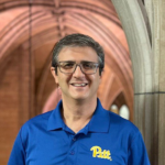 A man with short dark and grey hair wearing glasses and a blue polo shirt with the Pitt logo