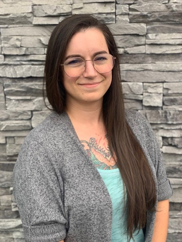 A woman with long dark hair and glasses wearing a gray sweater poses for a photo