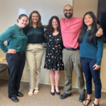 Group of four women and one man standing in a classroom smiling at the camera