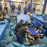 A group of students sit in a pit of blue foam blocks practicing putting a patient onto a spine board