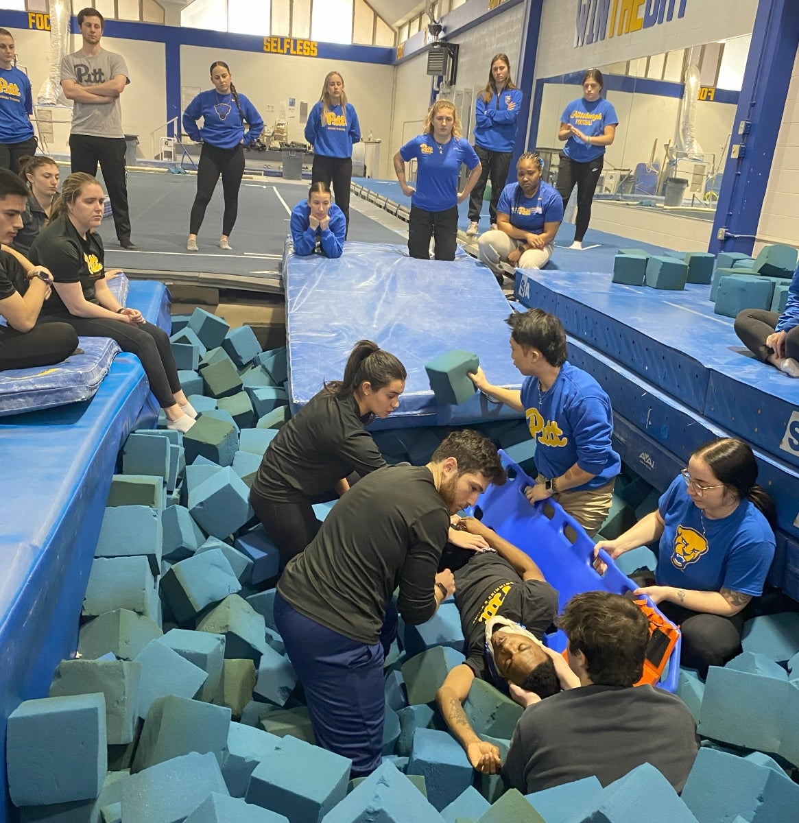 A group of students sit in a pit of blue foam blocks practicing putting a patient onto a spine board