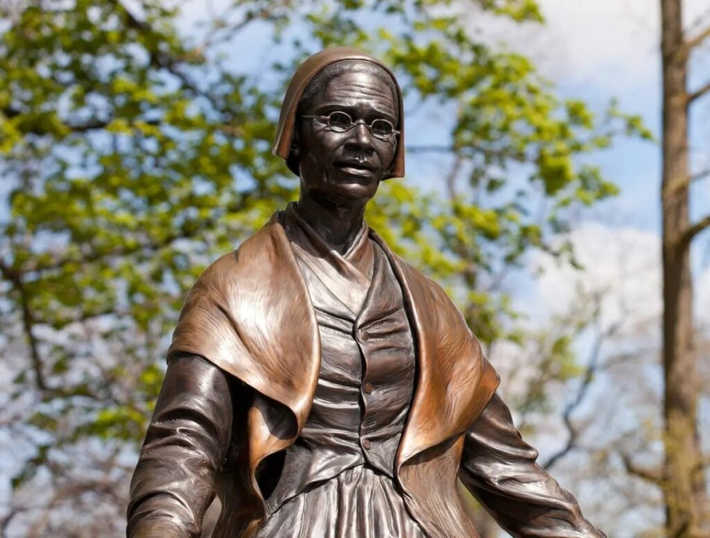 A statue of an older woman with a cap on her head and glasses wearing dress from the 1800s