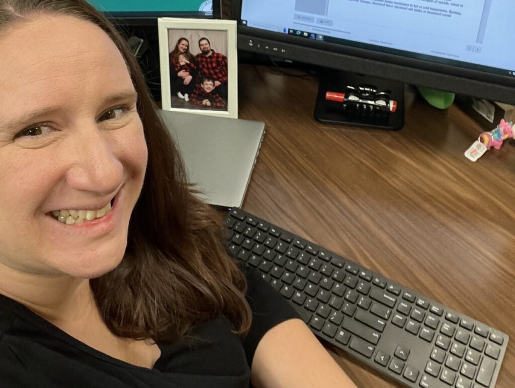 A woman sitting at a desk in front of a computer takes a selfie