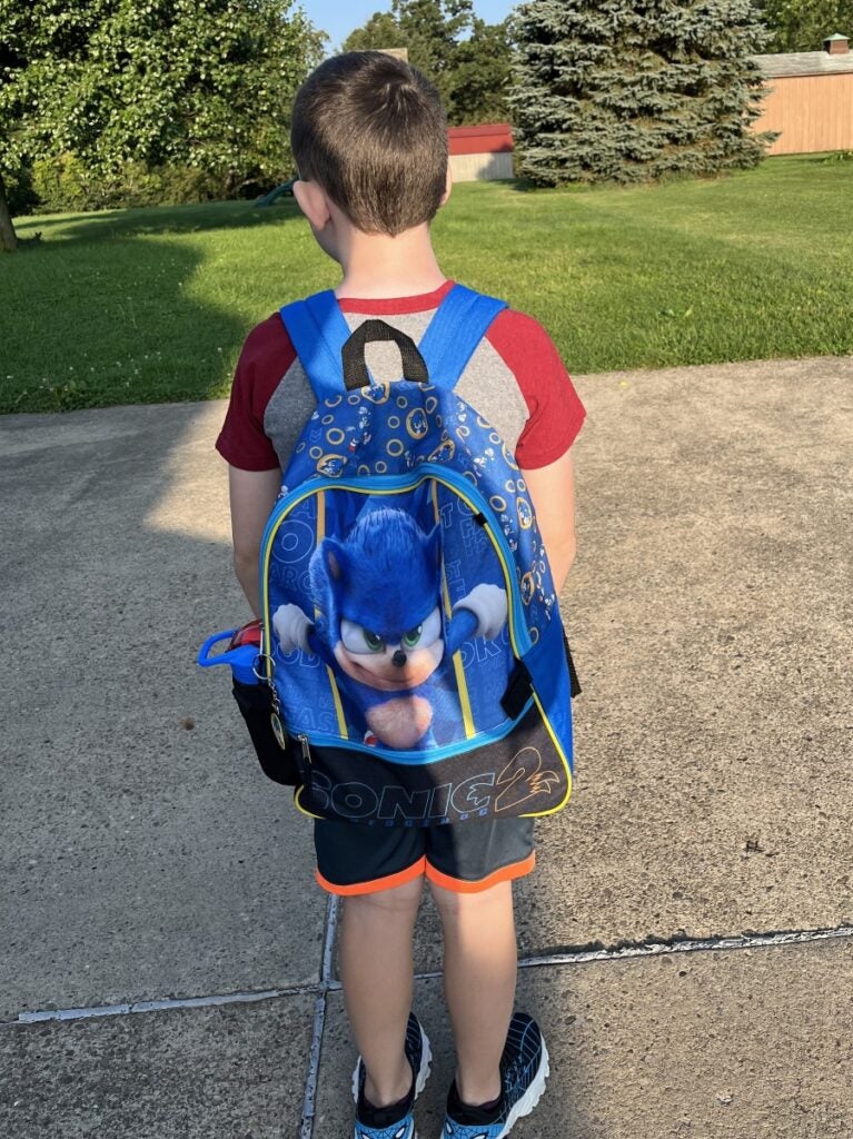 A boy with brown hair has his back turned to show a blue backpack with an animated character.