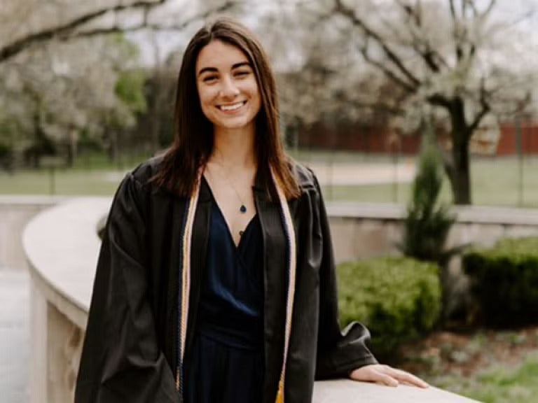 A woman with brown hair wearing a black graduation gown over a black dress.