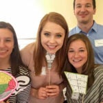 Three women and a man standing together holding graphics and diagrams related to communication science.