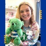 A woman with blonde hair holding a green teddy bear that wears a Thoracic-Lumbar-Sacral Orthosis around its torso.