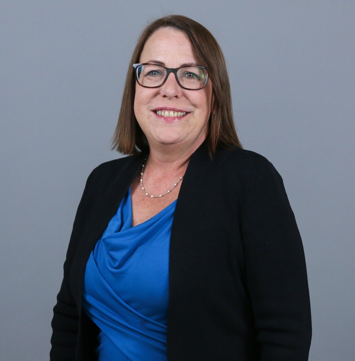 Woman with short brown hair wearing a black cardigan over a dark blue blouse and brown glasses.