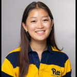 A woman with Asian features and long dark hair wears a blue and gold striped polo shirt poses for a photo