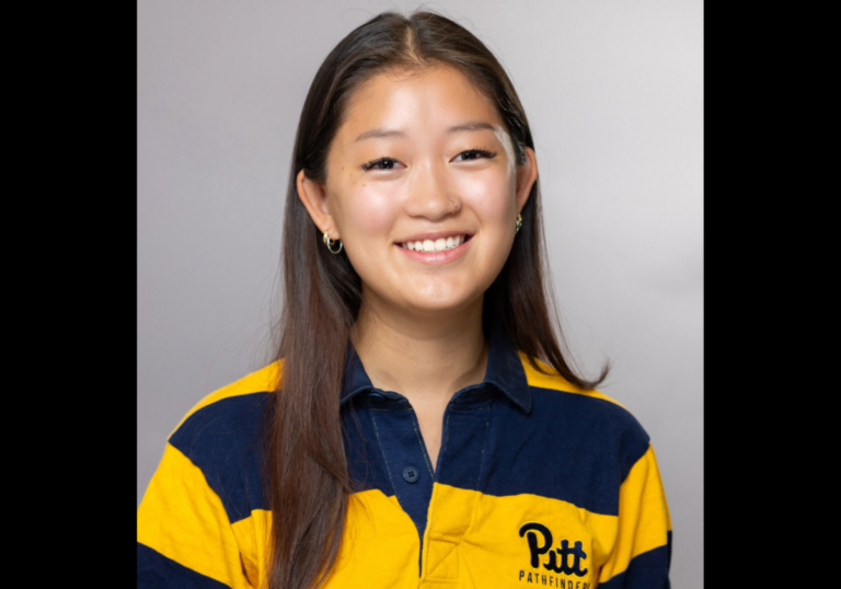 A woman with Asian features and long dark hair wears a blue and gold striped polo shirt poses for a photo