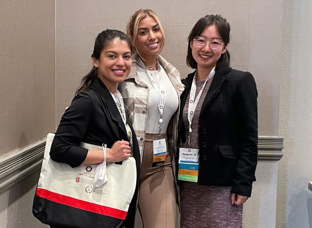 Three women standing together wearing conference badges smiling at the camera