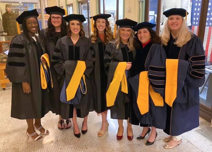 A group of seven women in graduation regalia pose together