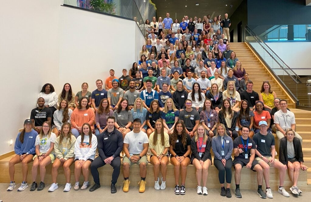 A large group of students sit in an atrium for a group photo