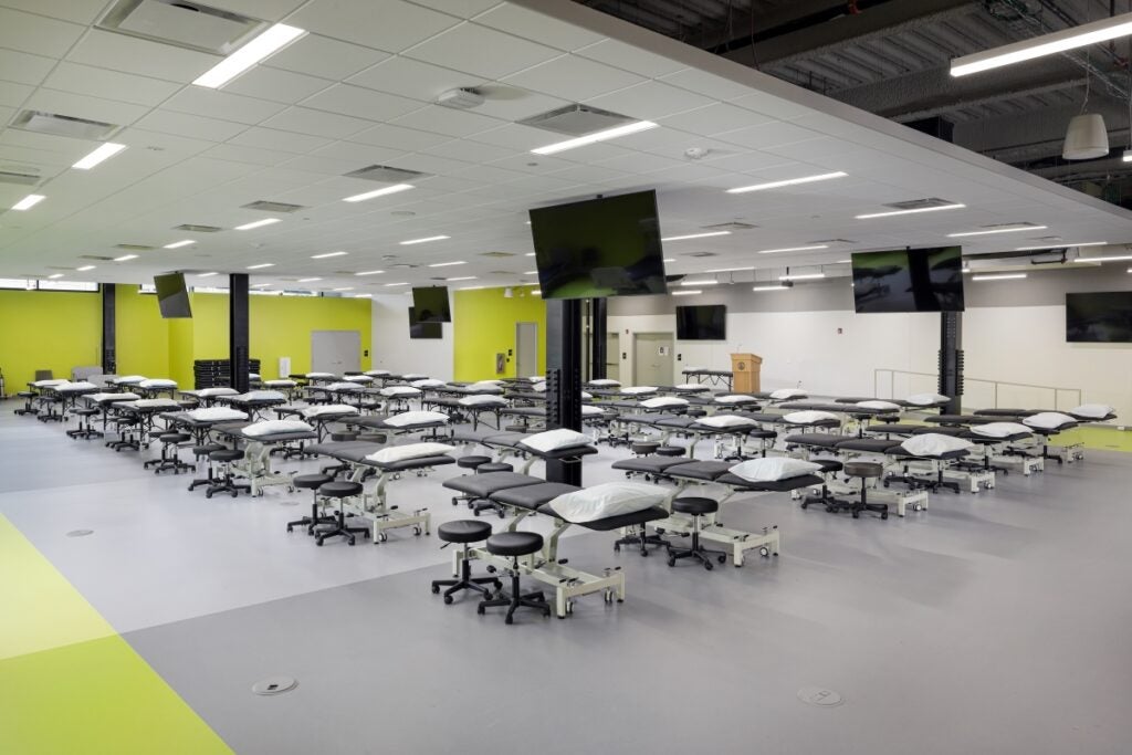 A large open room with dozens of patient tables, stools and flat screen televisions hanging from the ceiling.