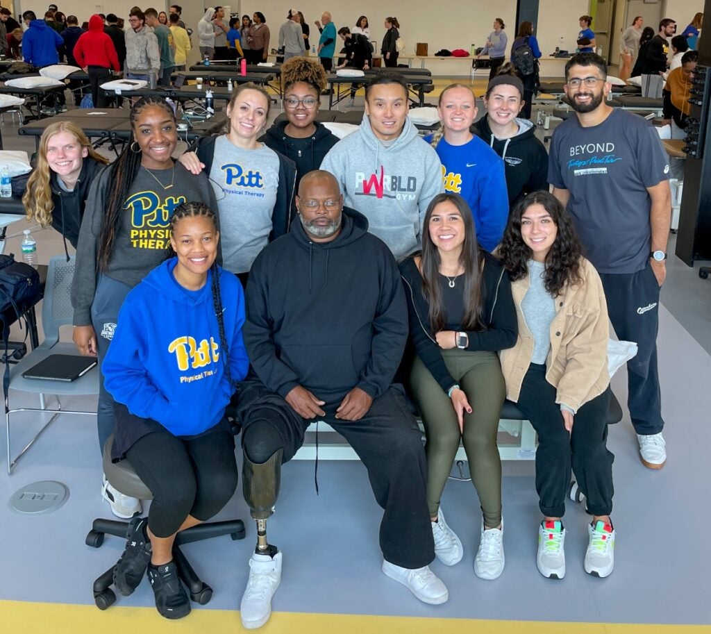 Eleven students sit around a man with dark skin and glasses and a right prosthetic leg.