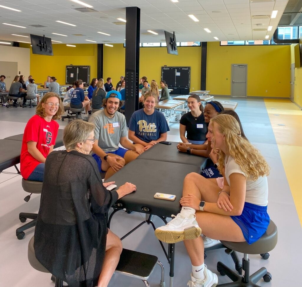 A group of seven students sit around a patient table talking with their instructor