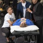 A professor demonstrates stretching a patient's leg as they lay on a table and two students watch