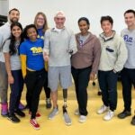 A group of students stand with a man with a prosthetic left arm and left leg