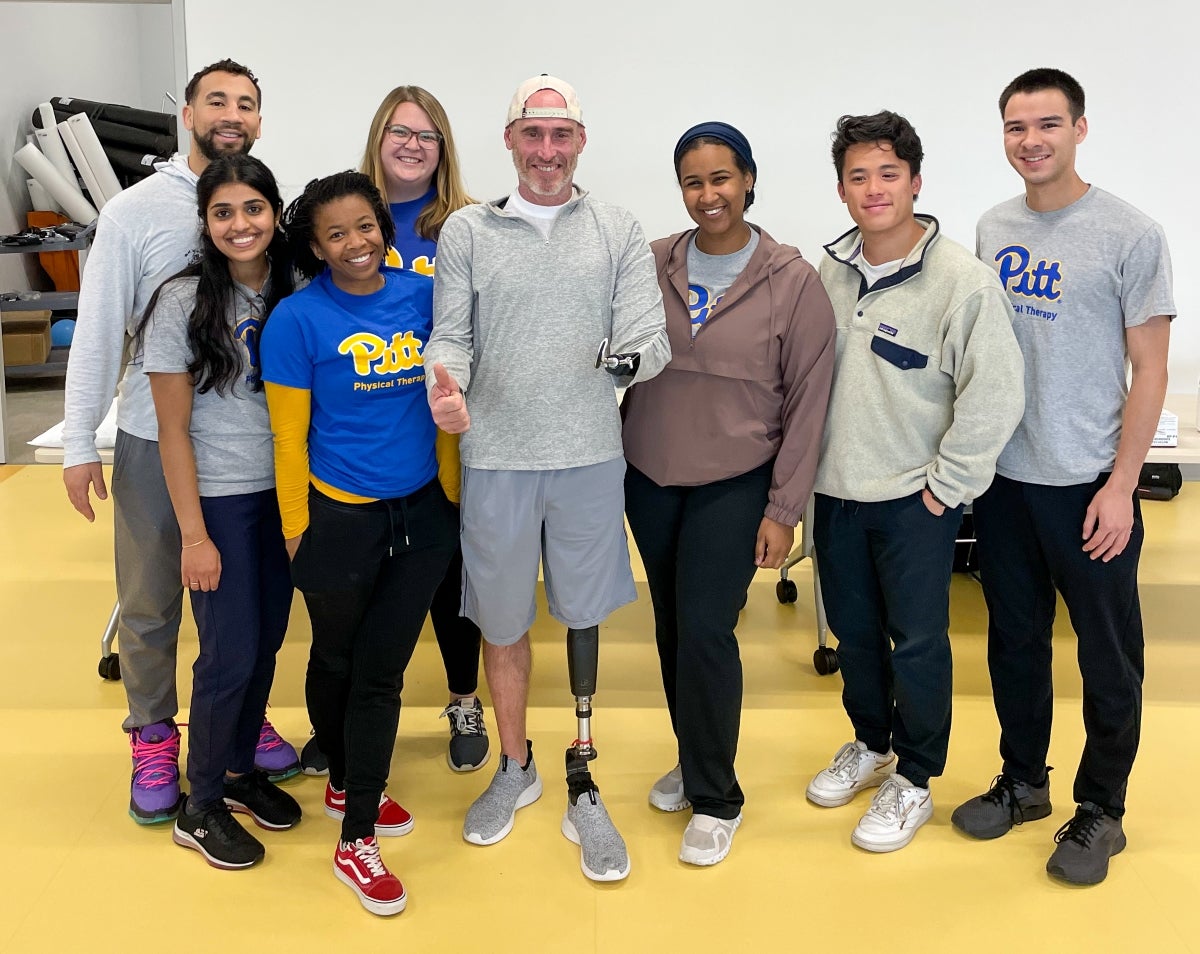 A group of students stand with a man with a prosthetic left arm and left leg