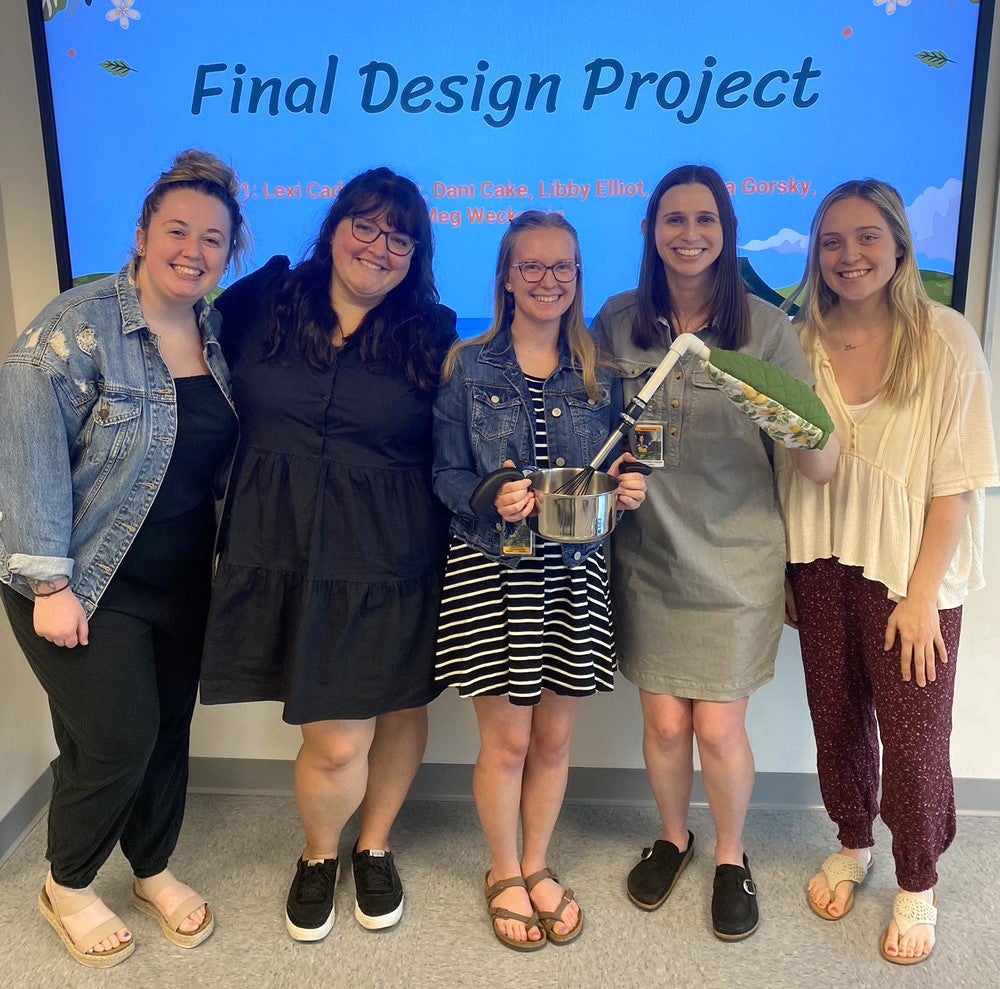 Five women stand in front of a presentation screen with the title Final Design Project