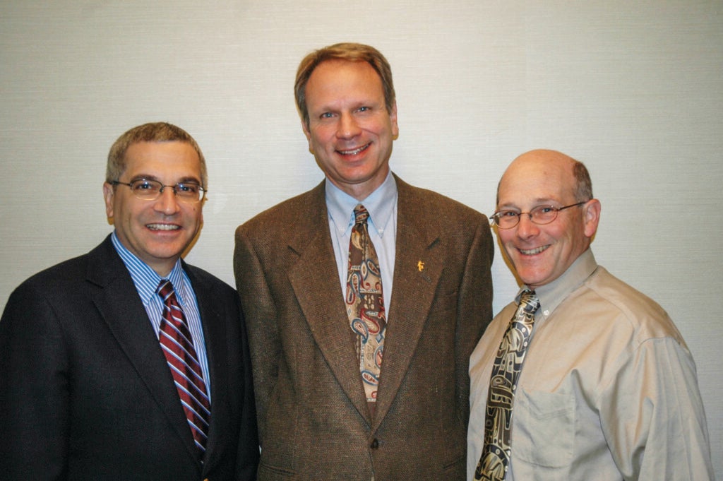 Three men standing together each wearing suit jackets, ties and collared shirts.