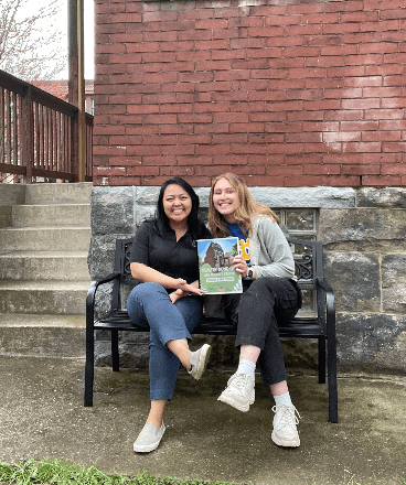 Denica Obis and Kayla Valente posing with a copy of the “Healthy Home Lab Age-Friendly Garden Toolkits and Case studies” handbook they created.