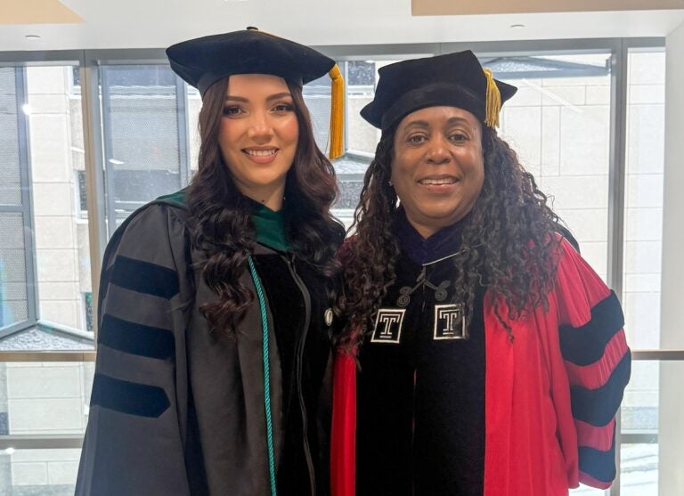 Two women in graduation regalia smile at the camera