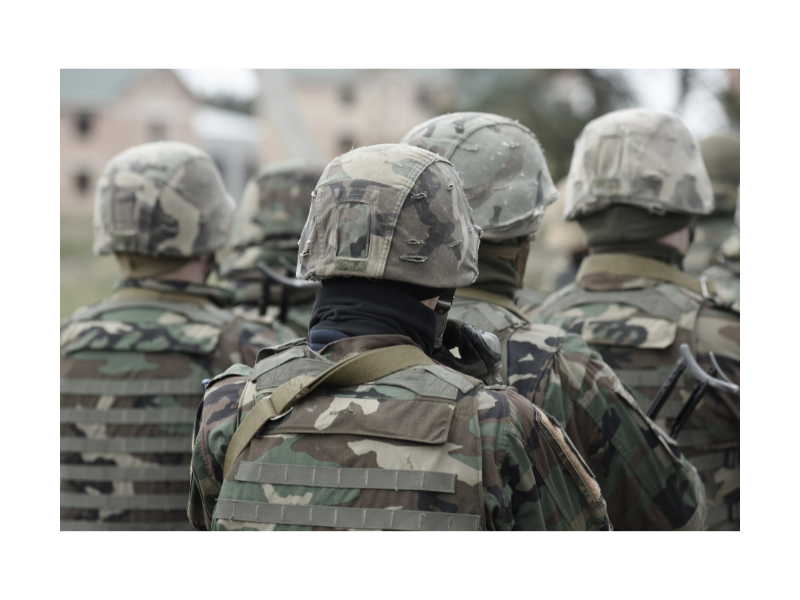 A group of military service persons wear camouflaged fatigues and helmets and face away from the camera