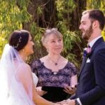 Bride and groom stand outside with woman officiant in the center.