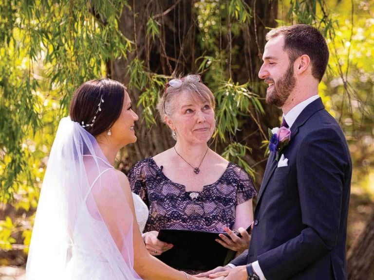 Bride and groom stand outside with woman officiant in the center.