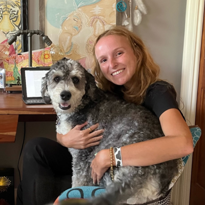 Woman with blonde hair sits in a chair holding a gray and white dog and smiles at the camera