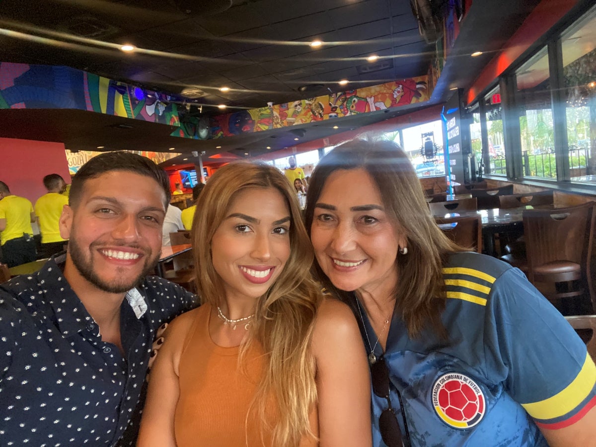 Three people in a colorful restaurant smile at the camera: a man in a polka dot shirt, a woman with long blond hair and woman with long dark hair