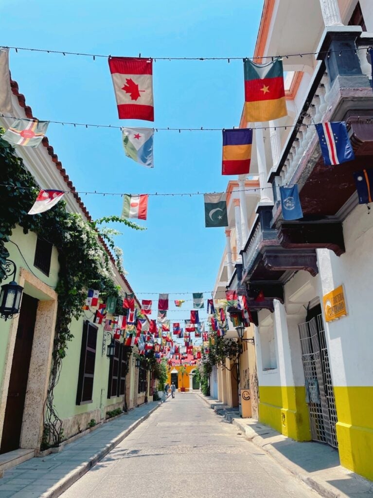 A narrow street divides colorful buildings on both sides, with flags of different countries hanging above the street