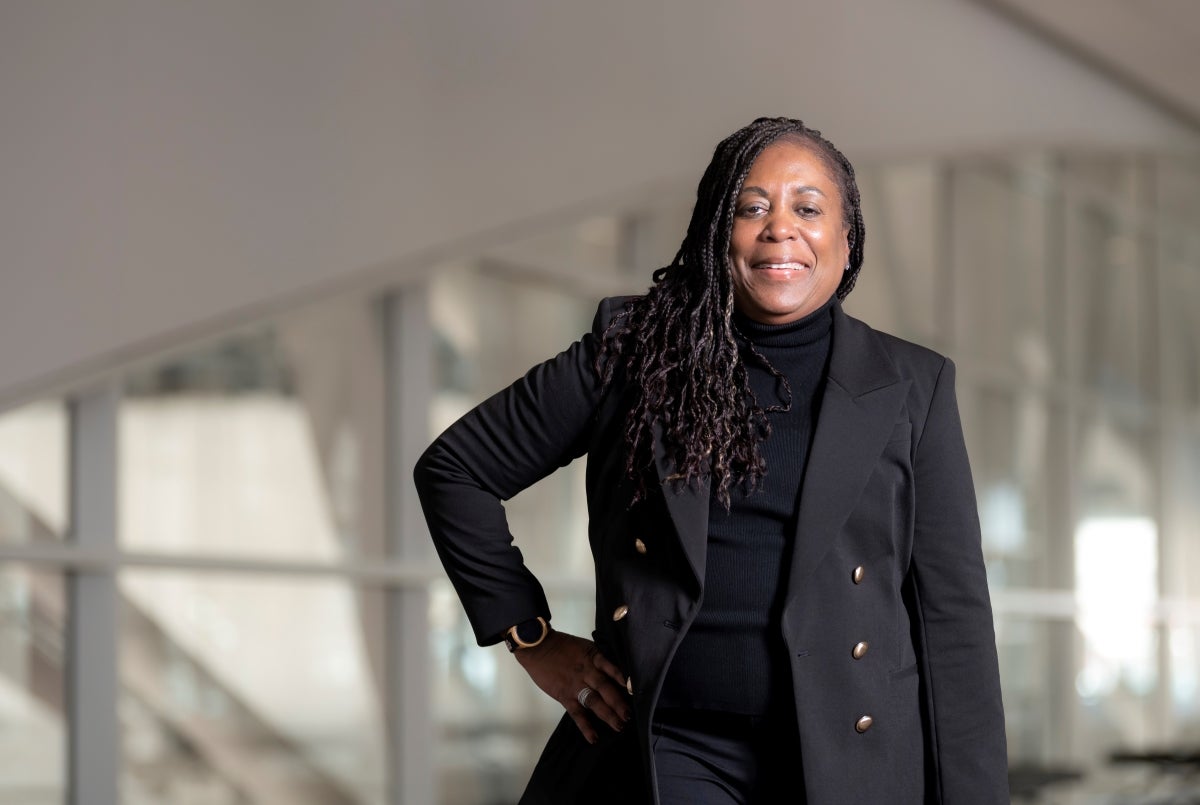 A woman with dark skin and long braided hair in a black suit poses for a photo