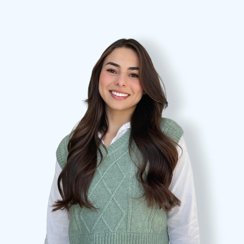 A woman with long brown hair wearing a sage green sweater vest over a white collared shirt.