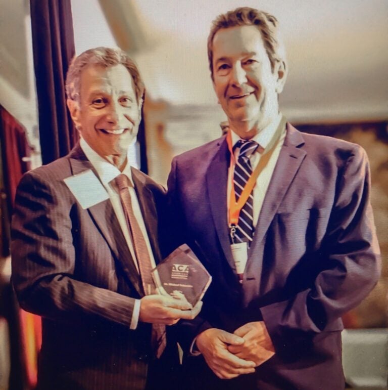 Two men in suits pose with one man holding a small crystal award