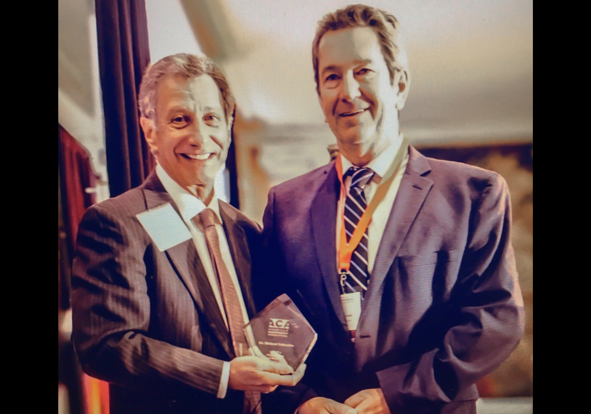 Two men in suits hold a small crystal award at a conference