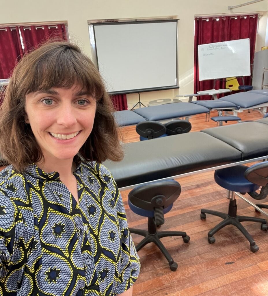 A woman with medium brown hair smiles in a selfie in a classroom with therapy tables and chairs