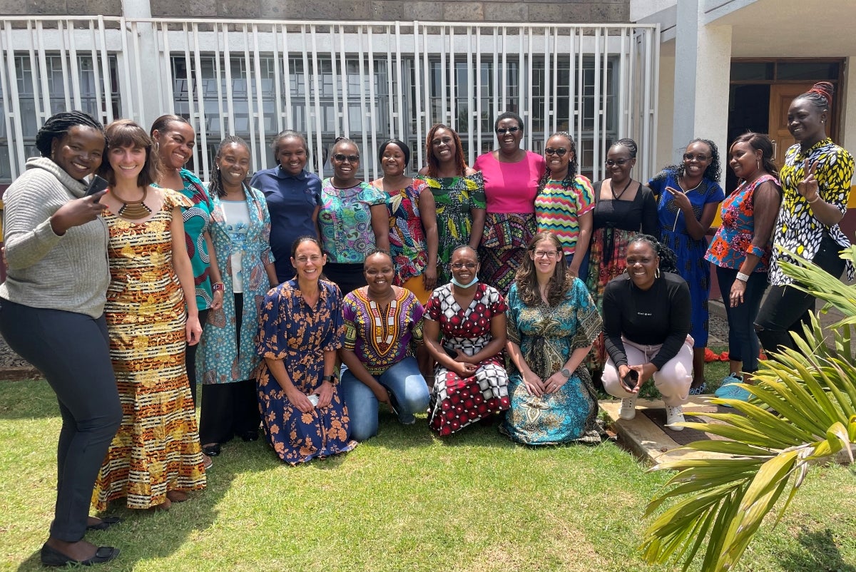 A group of women in colorful clothing stand and kneel smiling at the camera