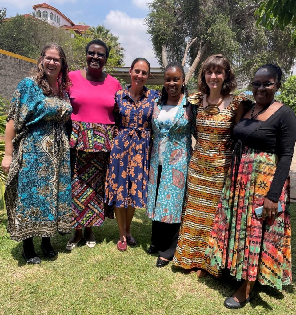 Six women wearing colorful dresses smile at the camera