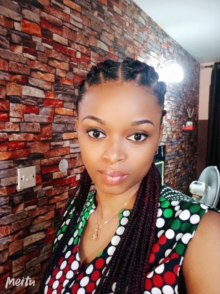 A woman with dark hair in braids wearing a black shirt with white, red and green polka dots.