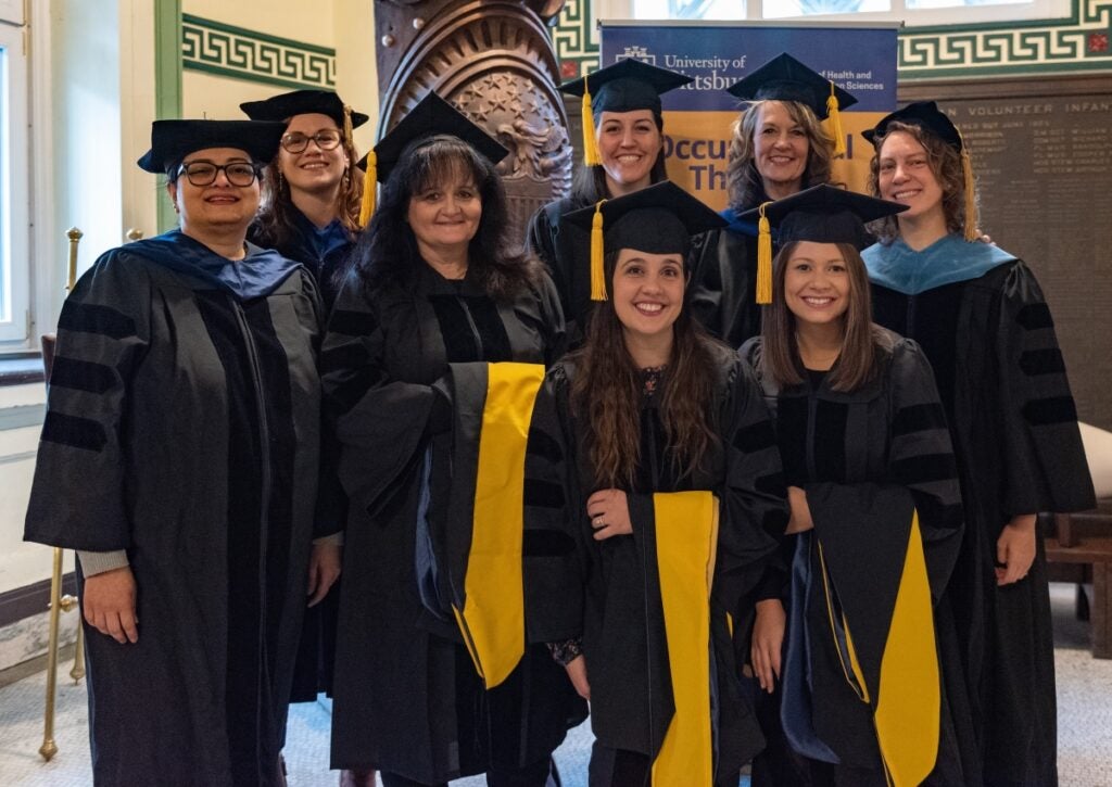 A group of eight women in graduation regalia smile at the camera