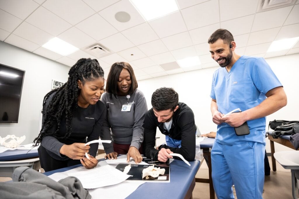 A group of four students look over a textbook while holding models of bone pieces