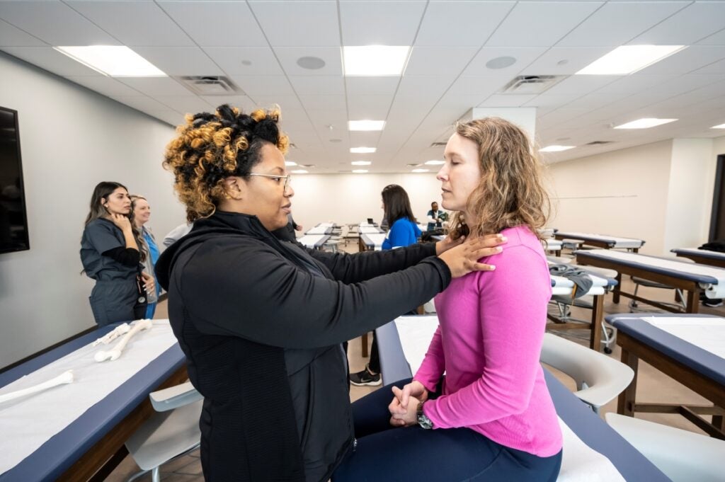 A woman with light brown skin and curly hair puts her hands on a patient's shoulders