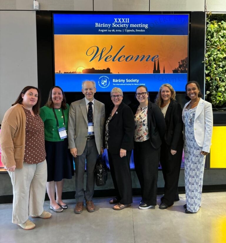 A group of seven people stand in front of a conference welcome sign