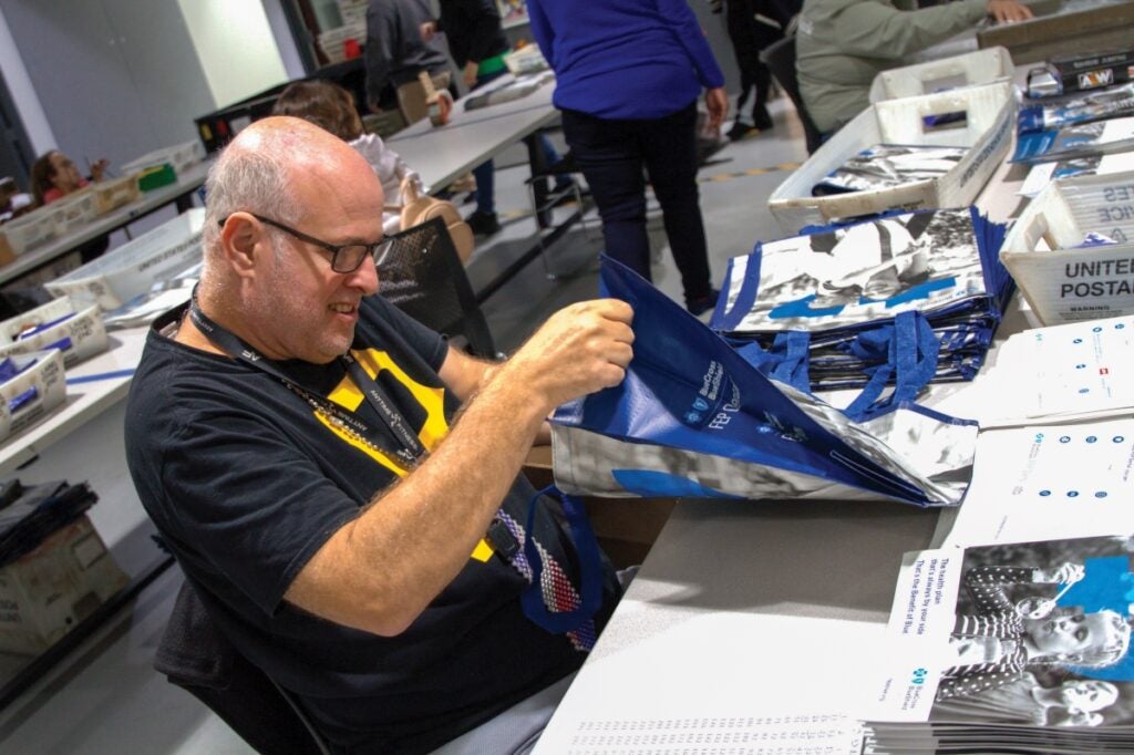 A man with thin gray hair and glasses sits at a table while opening a bag