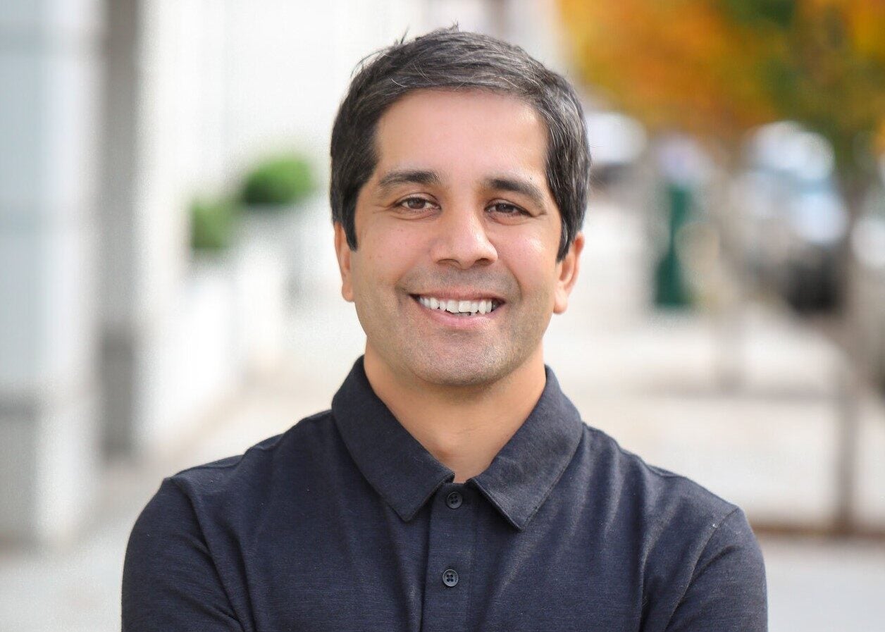 A man with short dark hair wearing a black collared shirt.