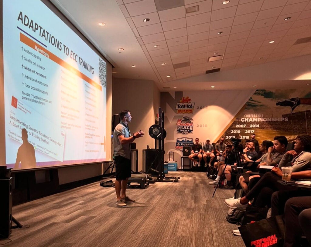 Tim Suchomel standing in front of an audience with a presentation screen behind him