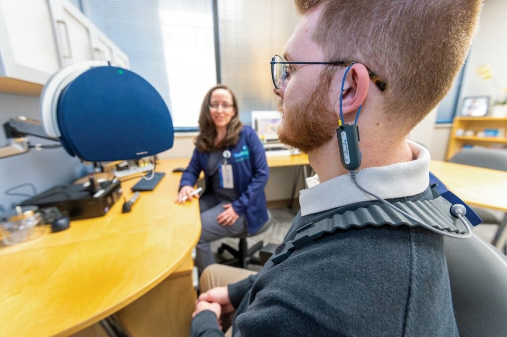 A man sitting in a chair has a testing device looped on his left ear