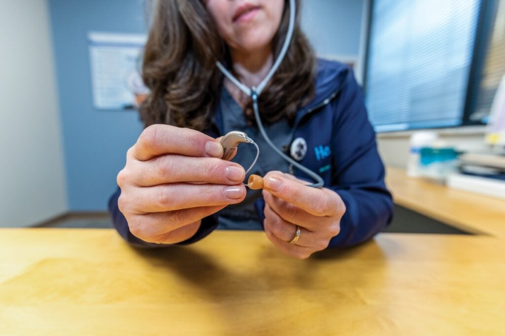 A woman sitting in a chair holds a small hearing device in her hands